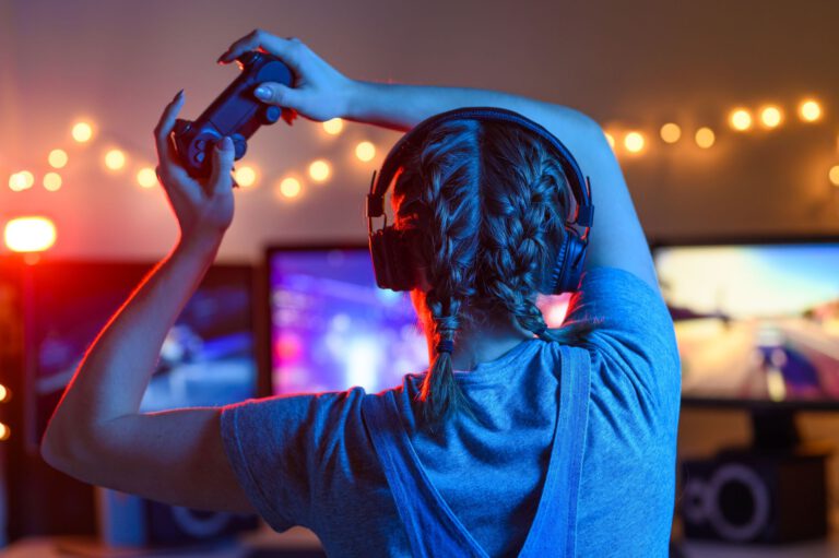 Gamer or streamer girl at home in a dark room with a gamepad playing video games with friends online. Young man sits in front of a monitor